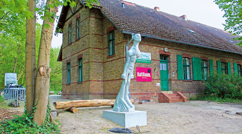 Mit seiner neuen Heimat hat er das große Los gezogen: Direkter Blick auf den Machnower See, alle Menschen schauen zu ihm auf – nur eine Frau fehlt ihm noch zu seinem Glück. Die Rede ist vom „großen schrägen Mann“, einer neuen Steinskulptur vor dem Landarbeiterhaus im Zehlendorfer Damm 200 in Kleinmachnow, die am 22. April von Gemeindebürgermeister Michael Grubert, Rainer Ehrt, dem Vorsitzenden des Kunstvereins „Die Brücke“, und weiteren Kulturinteressierten als neues Wahrzeichen der märkischen Kulturlandschaft eingeweiht wurde.